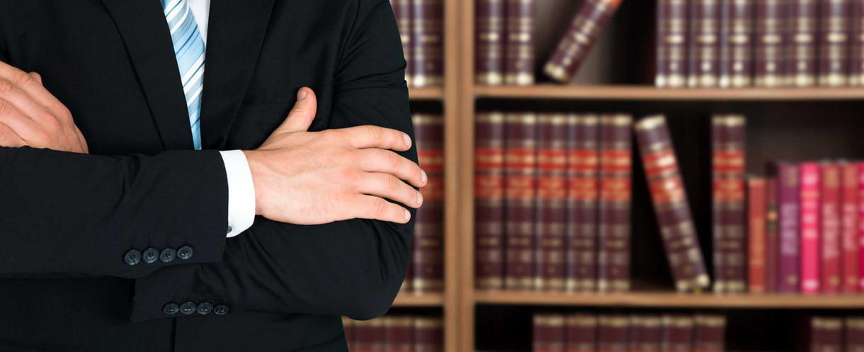 Person stands with folded arms in front of shelf with law books.